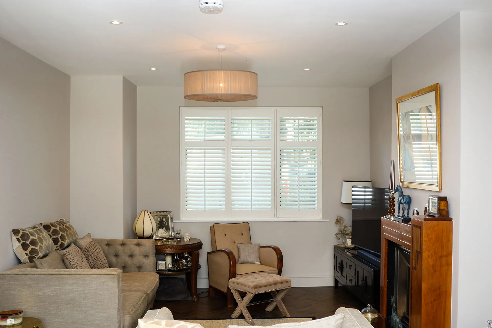 Cozy living room featuring a light fixture, beige sofa with patterned cushions, an armchair, and a TV stand with decorative pieces.